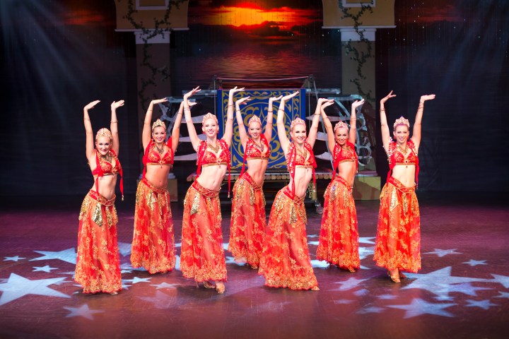 Women on stage dressed in Indian bellydancer costumes with hands upraised